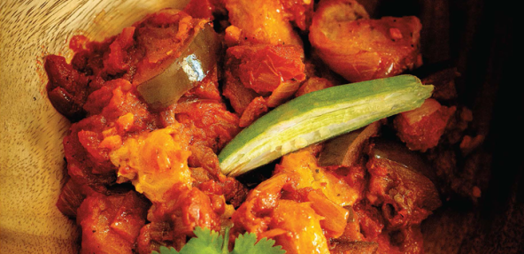 Plantain and eggplant stew, served in a wooden bowl with a garnish of corriander and green chili