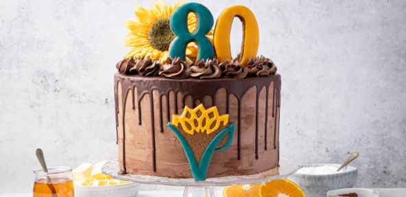 The Vegan Society 80th anniversary chocolate, orange and ginger cake on a stand displayed around ingredients