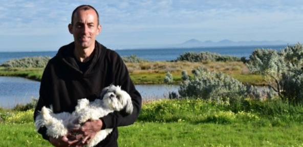 Vegan Society Volunteer, Lee Hawkins outdoors holding his rescue dog.