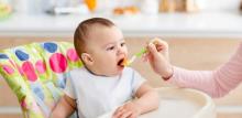 Mother giving healthy food to her baby in the kitchen