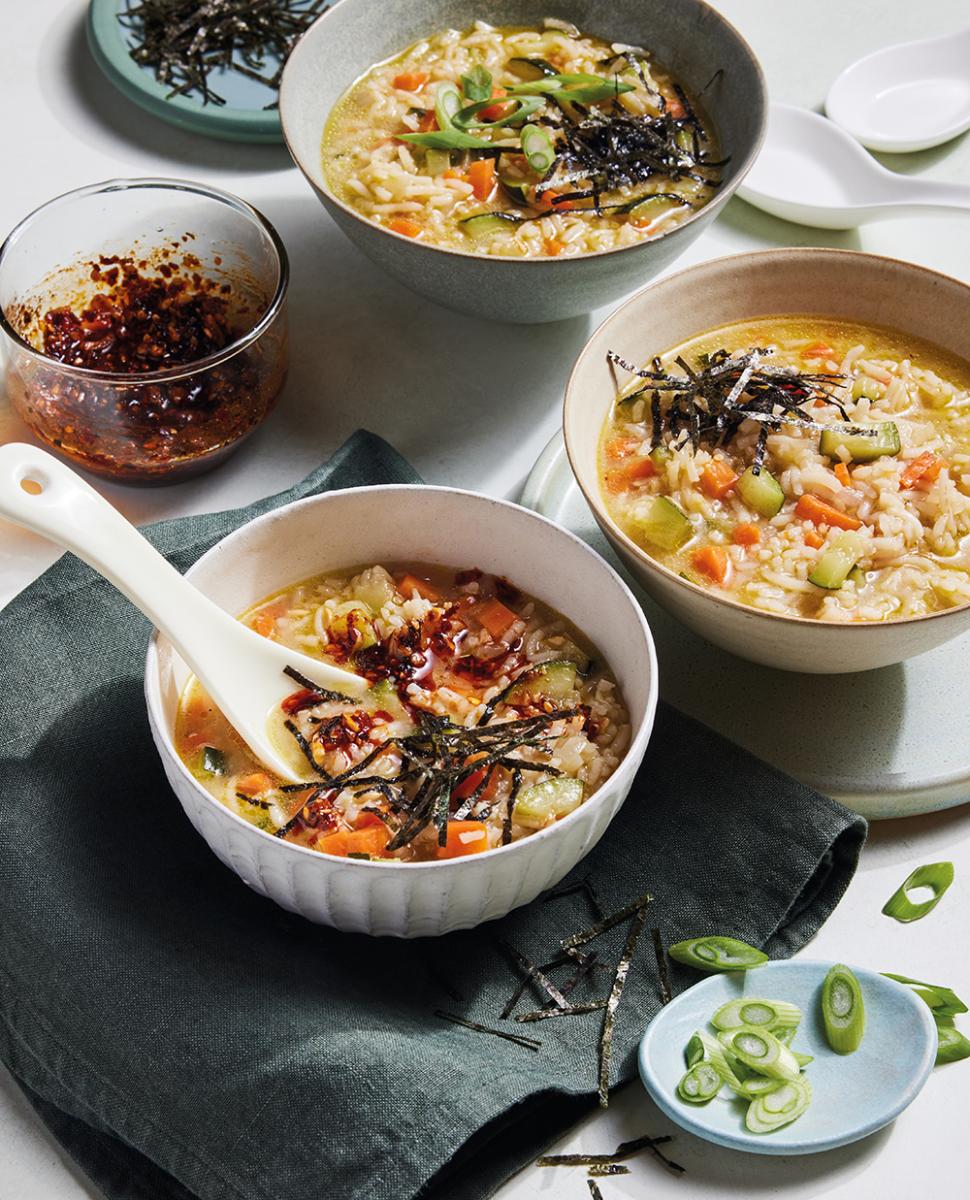 A bowl of Korean porridge with garnish of seaweed strips, chilli jam and spring onions.