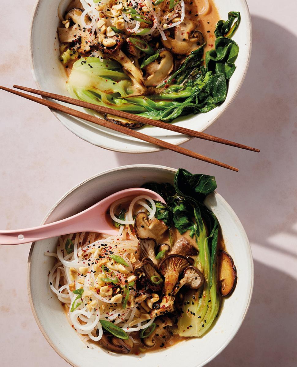 Spicy peanut ramen in bowls of green vegetables and mushrooms with chopsticks rested on the side.