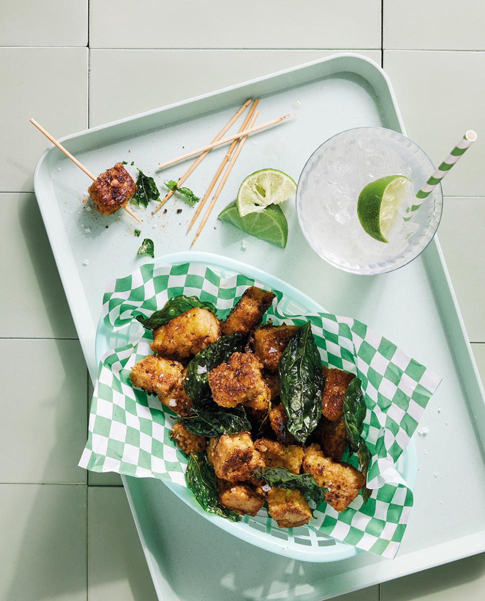 A food basket lined with checked green and white paper and filled with popcorn tofu with a garnish of lime on the side.