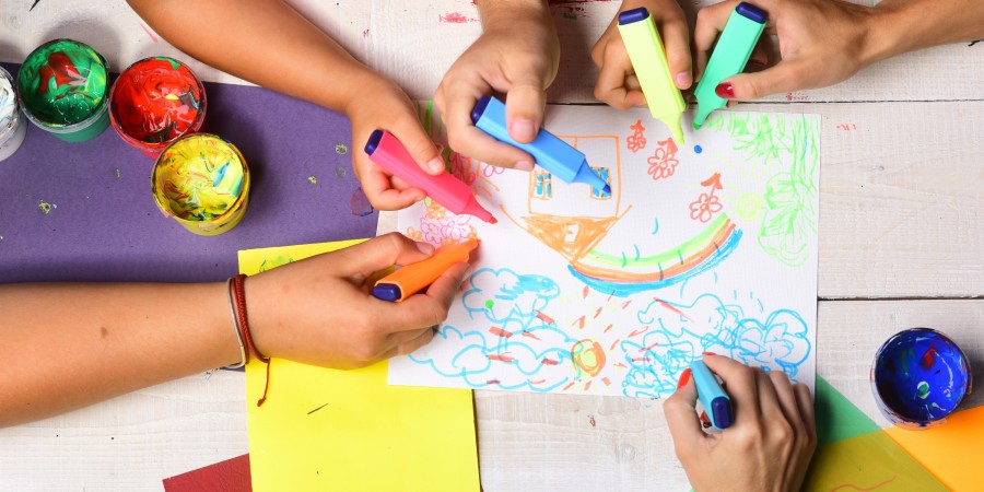 Group of children holding highlighter pens and colouring in, surrounded by paint pots and crafts