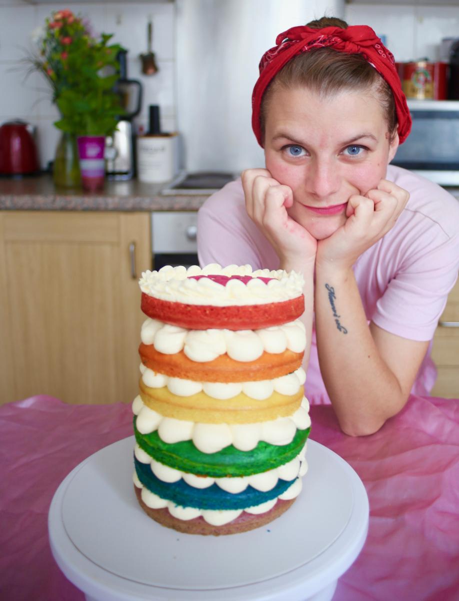 The Female Glaze baker Francesca standing next to a rainbow cake