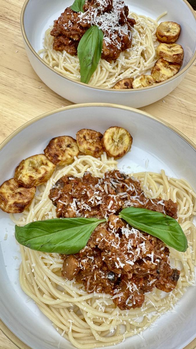 Jollof Spaghetti Bolognese with walnuts and mushroom served on a plate with garnish