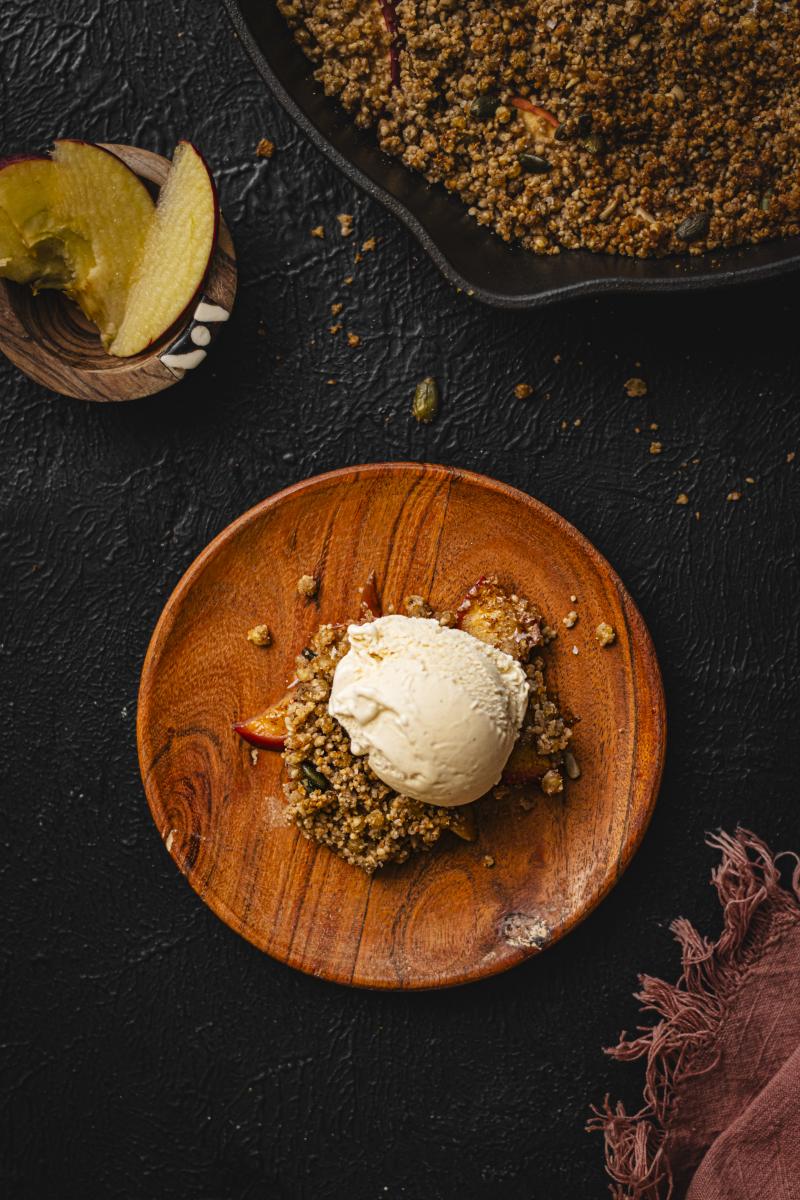 This is an image of sorghum apple crumble in a bowl, next to a pot of sliced apple and a large pan of crumble. 