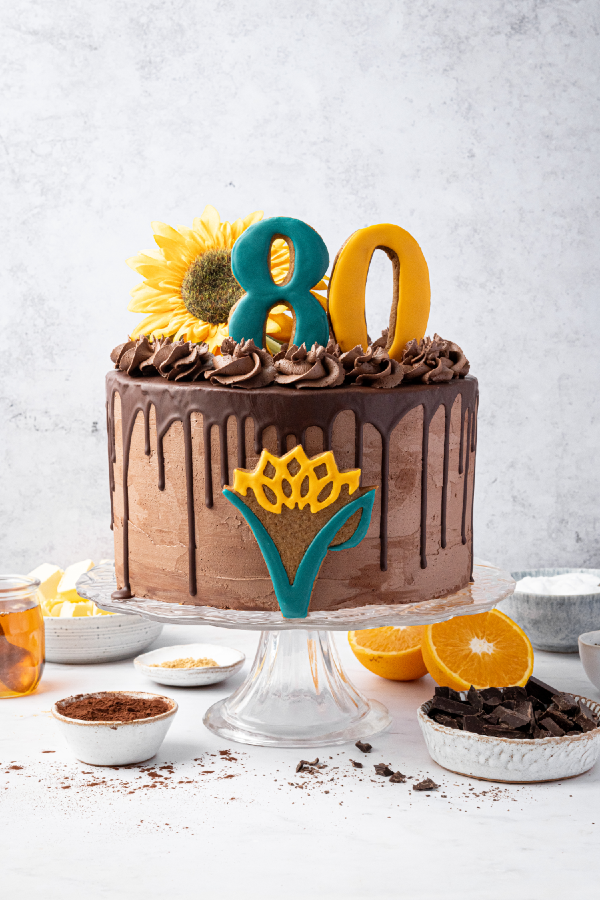 The Vegan Society 80th anniversary chocolate, orange and ginger cake on a stand displayed around ingredients