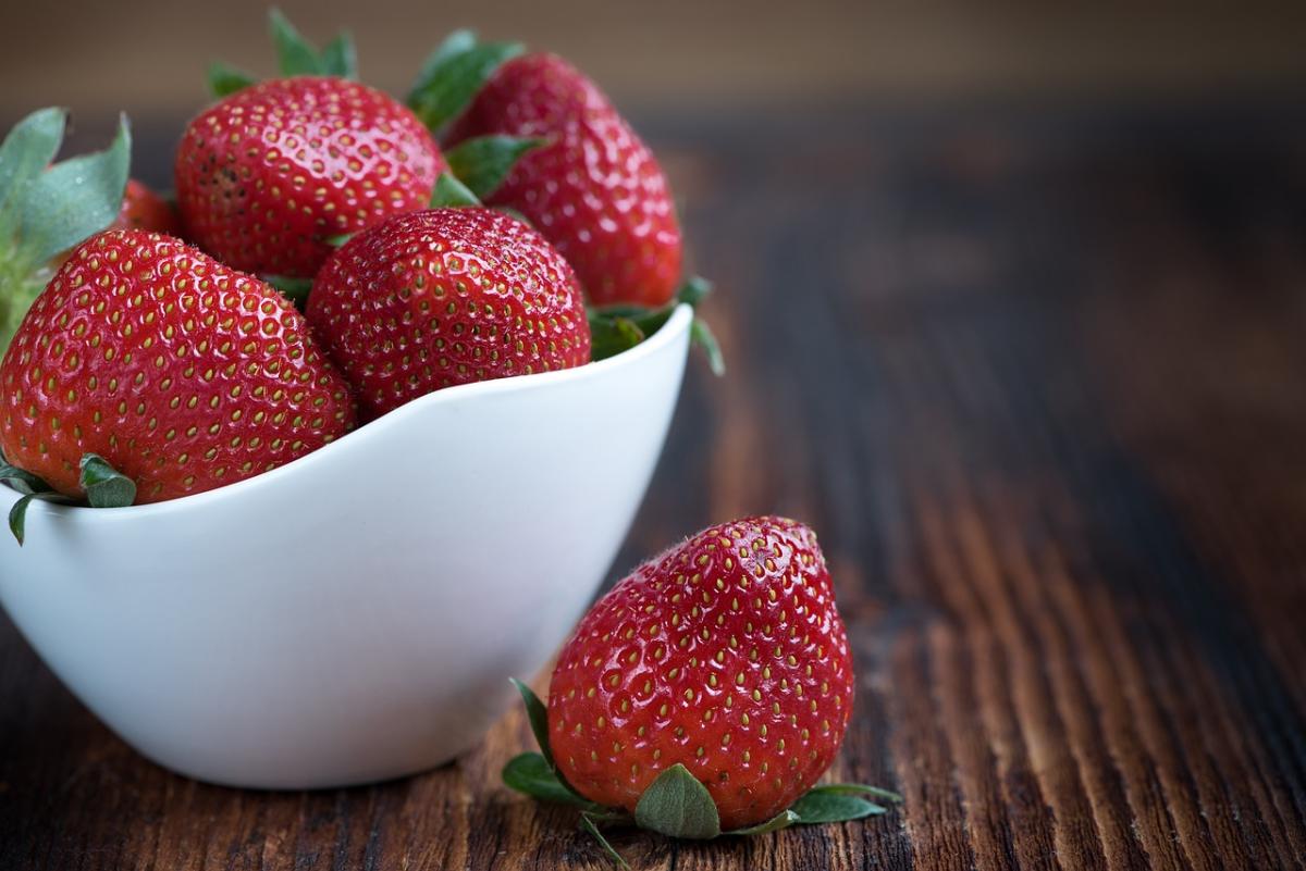 Strawberries in a white fruit bowl on a wooden surface. 